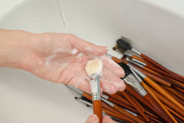 woman is washing dirty makeup brush with soap and foam in the sink - make up brush imagens e fotografias de stock