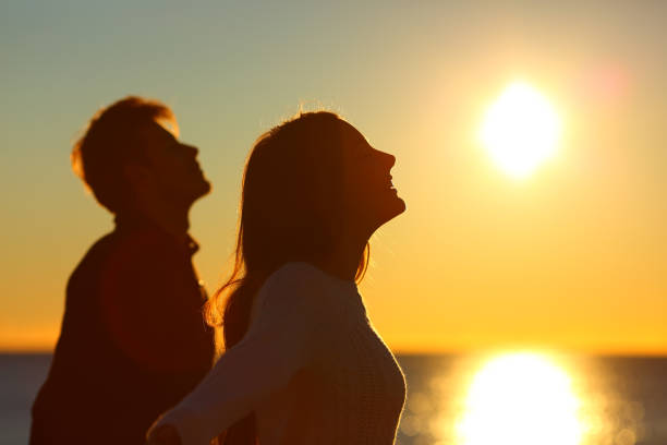 Silhouette of a couple of friends breathing at sunset Silhouette of a couple of friends breathing deep fresh air at sunset on the beach tranquil evening stock pictures, royalty-free photos & images