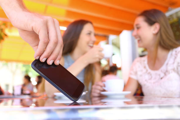 Distracted friends talking in a bar and close up of a thief hand stealing phone on foreground
