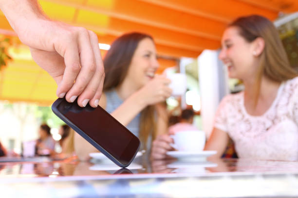 Distracted friends talking in a bar and thief stealing phone Distracted friends talking in a bar and close up of a thief hand stealing phone on foreground pickpocketing stock pictures, royalty-free photos & images