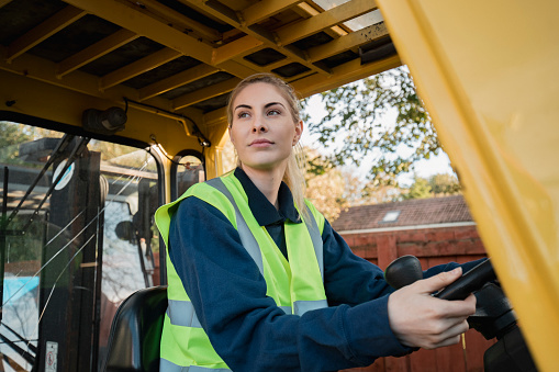 A close-up shot of a female manual worker driving a forklift, she looks confident and ready for the day ahead.