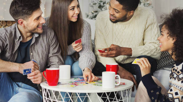 Happy friends playing game of cards UNO Multiracial friends having fun and playing game of cards UNO against christmas tree friends playing cards stock pictures, royalty-free photos & images