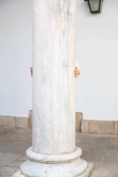 Photo of litlle child behind ancient column peeking hands