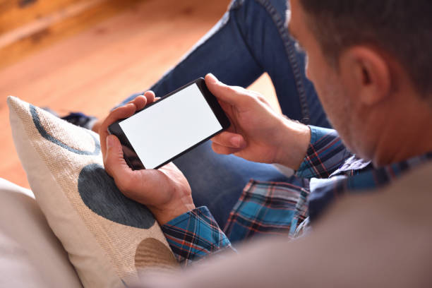 mann sitzt auf dem sofa beobachten multimedia-inhalte auf einem smartphone - horizontal stock-fotos und bilder