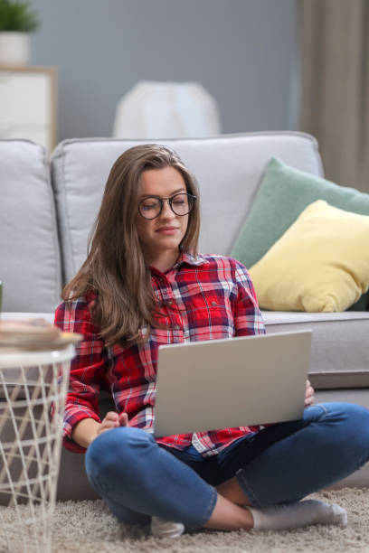istock Portrait of a smiling female  in glasses using laptop computer while relaxing on a couch at home. 1063736146