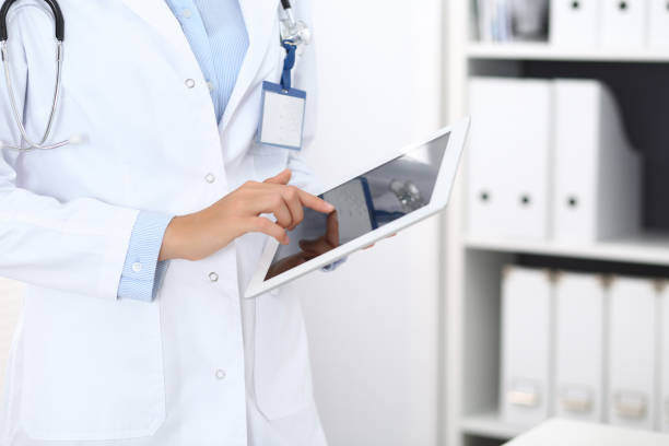 istock Doctor woman using tablet in clinic office. Unknown female physician at work while standing straight at hospital, close-up. Medicine and healthcare concept. 1063739666