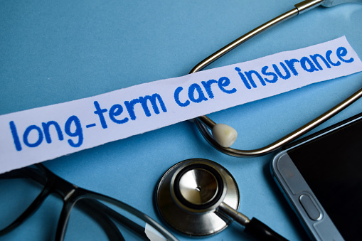 Conceptual image with Long-term care insurance inscription with the view of stethoscope, eyeglasses and smartphone on the blue background. Medical Conceptual.