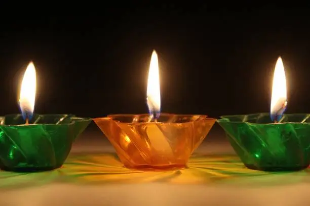 Group of burning candle-lights in coloured ( red, yellow and green) glass candle-holders, neutral background, Dark background, blurred, bokeh effect and light dots. No person. Space for text. festival