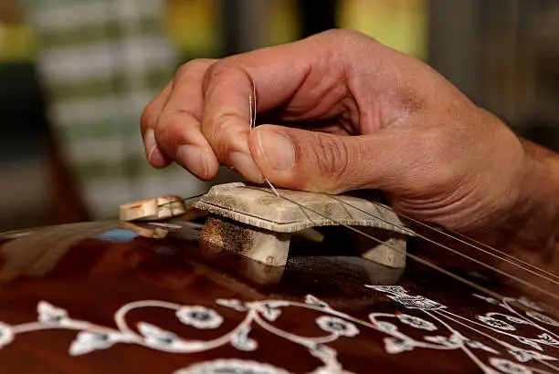Fingers delicately adjusting the strings of a 'thaanpura'.