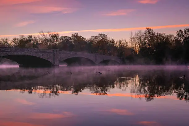 Misty autumn sunrise over Carnegie lake in Princeton, New Jersey featuring old bridge on the background