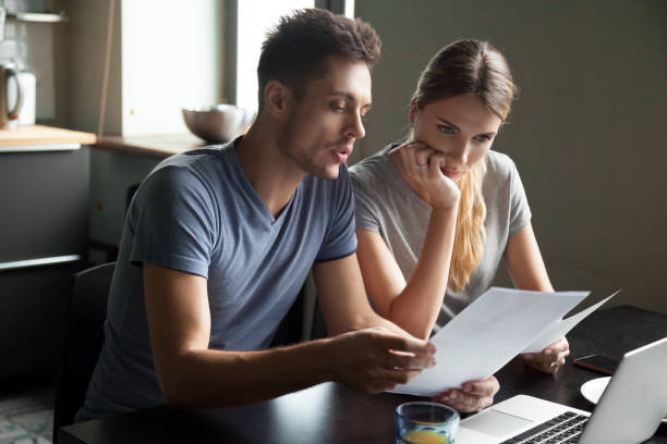 poważna młoda para sprawdza dokumenty za pomocą laptopa - bill couple finance debt zdjęcia i obrazy z banku zdjęć