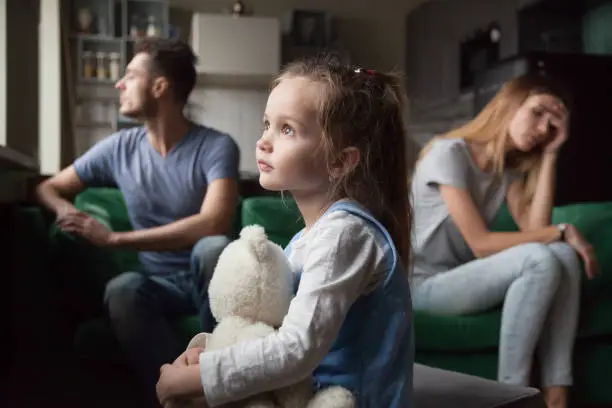 Upset frustrated little girl tired of parent fight, toddler daughter holding toy dreaming that family conflicts would stop, suffering from mother and father quarrels, bad family relationship, break up