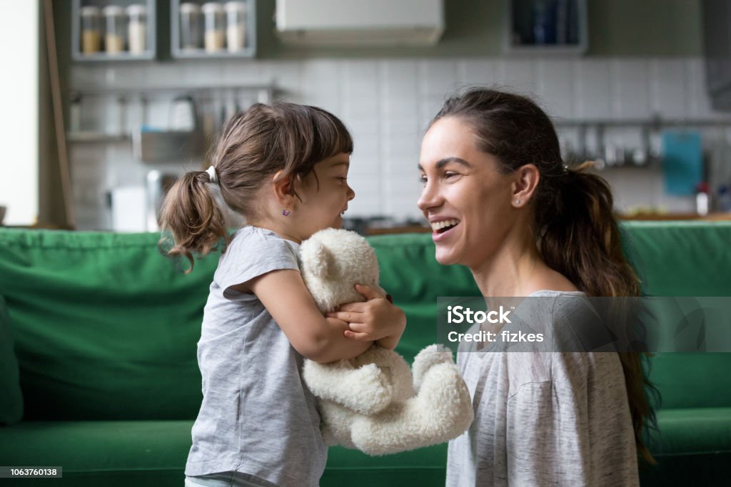 Smiling young mum talking with little daughter Smiling young loving mum talking with little preschool daughter with favorite stuffed toy, playing in living room at home, mother laughing with child, babysitter playing with pupil Child Stock Photo