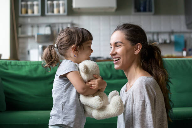 Smiling young mum talking with little daughter Smiling young loving mum talking with little preschool daughter with favorite stuffed toy, playing in living room at home, mother laughing with child, babysitter playing with pupil obedience photos stock pictures, royalty-free photos & images