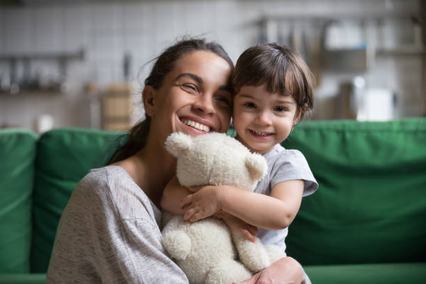 Smiling single young mum embracing little daughter Smiling single young mum embracing little preschool daughter with toy, playing in living room at home, mother laughing with child, headshot portrait, cute girl look at camera nanny photos stock pictures, royalty-free photos & images
