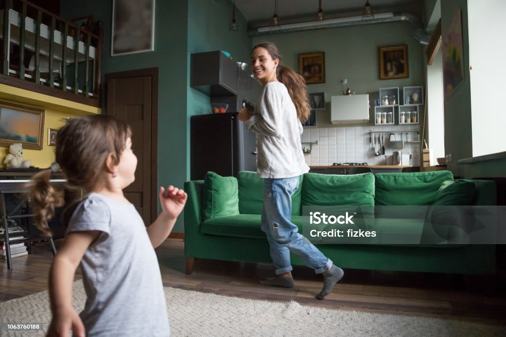 Happy excited single mother playing with daughter Happy excited smiling fit single mother running with little preschool cute daughter in living room at home, babysitter playing with girl, pupil, family spending time together, having fun Running Stock Photo