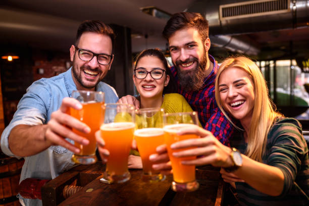 Group of young friends in bar drinking beer toasting the camera Friends in Pub drinking Beer having Fun celebratory toast photos stock pictures, royalty-free photos & images