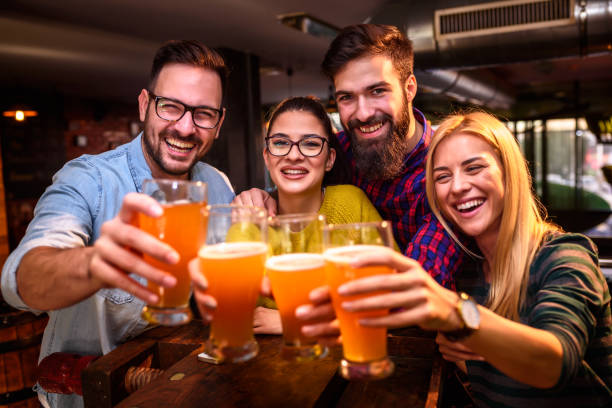 group of young friends in bar drinking beer toasting the camera - beer pub women pint glass imagens e fotografias de stock