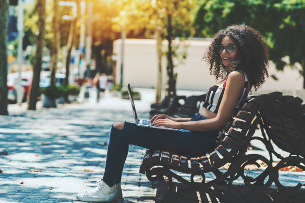 istock Cheerful curly female with laptop on the bench 1063769414