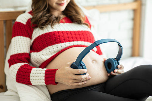 Young Attractive Asian pregnant woman listen music and lying on bed in the room.Pregnant woman use headphones to play classical music for child learn and Development feeling so relax and comfortable