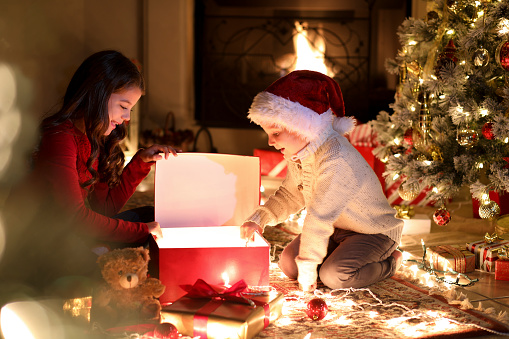 Children open gifts during Christmas season.  Christmas tree, lights, fireplace.