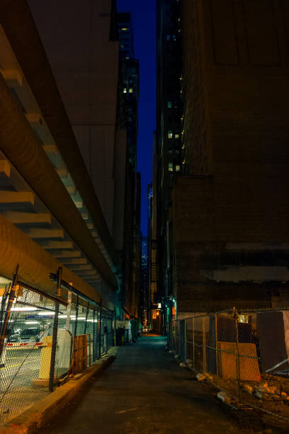 dark and scary downtown urban city street alley next to an eerie illuminated parking garage and spooky empty lot at night - street light parking lot night lot imagens e fotografias de stock
