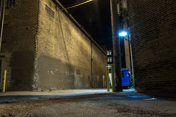 Dark and scary downtown urban city street corner alley with an eerie vintage industrial warehouse factory and a dirty dumpster at night Dark and scary downtown urban city street corner alley with an eerie vintage industrial warehouse factory and a dirty dumpster at night alley stock pictures, royalty-free photos & images