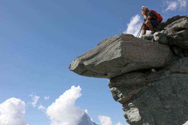 istock Man sits on top of rock overhang, mountains below 1063792662