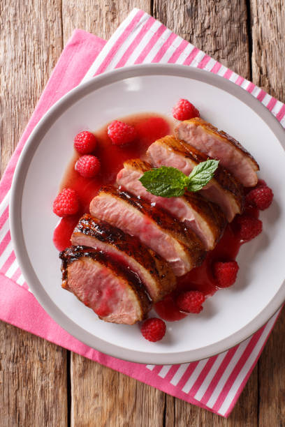 istock natural food: fried duck breast served with fresh raspberry sauce and mint closeup on a plate. Vertical top view 1063820582