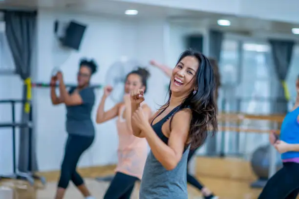 A beautiful woman looks into the camera laughing while she dances in this fitness class. She is surrounded by her friends who are doing the same.
