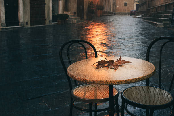 Parisian cafe terrace in rainy autumn day. Rain drops and maple leaf on the table.