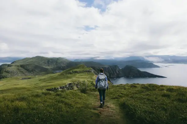 Woman with backpack hiking through beautiful hills near sea in Norway
