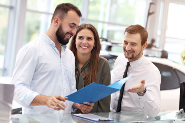 istock Confident young salesman explaining car features to the young attractive owners 1063843174