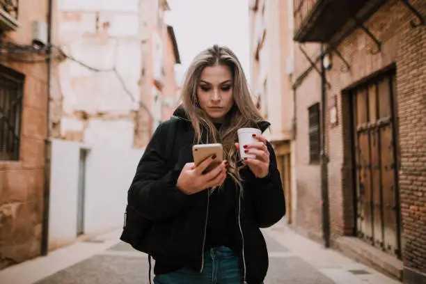 A young woman with a coffee-to-go cup in a city, looking at her smartphone