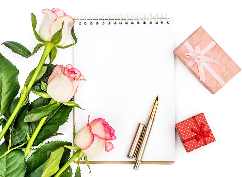 Bunch of roses with blank notepad and gift boxes on white. Top view.