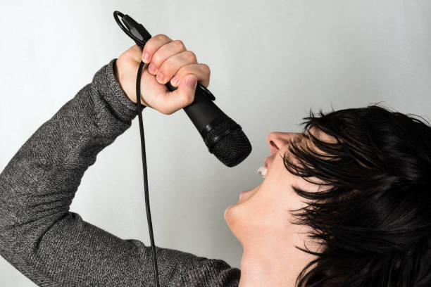 screaming in microphone The young black hair guy is singing or screaming in the microphone on gray background. emo stock pictures, royalty-free photos & images