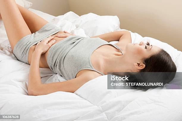 Female Holding Stomach While Laying In Bed Stock Photo - Download Image Now - Lying Down, Human Abdomen, One Woman Only