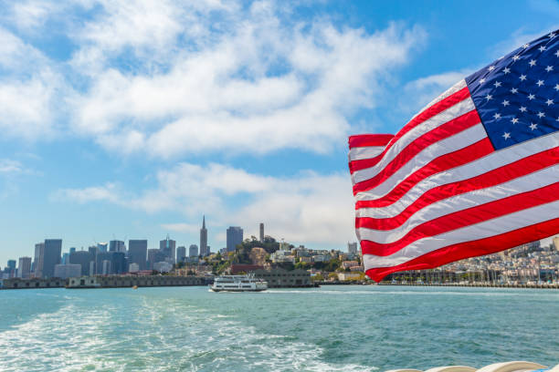 San Francisco, California, United States - August 14, 2016: american flag in San Francisco Bay cityscape. Tour to Alcatraz island by ferry boat waving in San Francisco pier with cityscape. Cloudy sky.