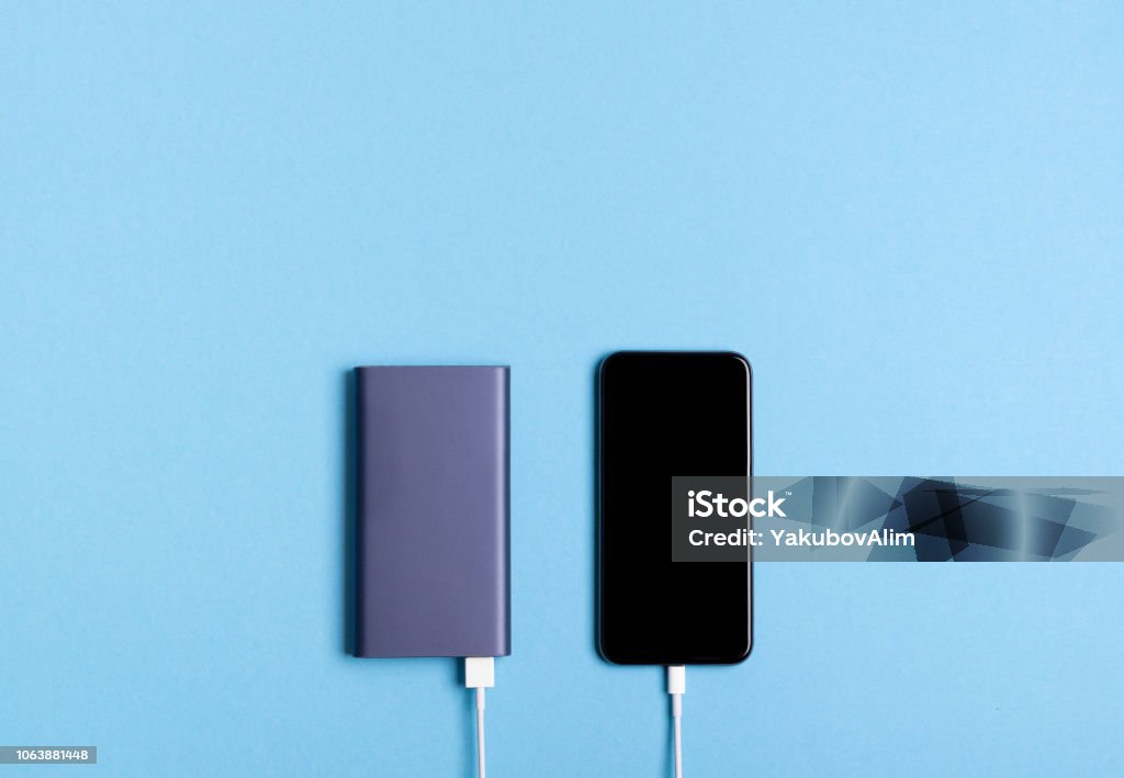 Smartphone charging with power bank on blue background Power Bank Stock Photo