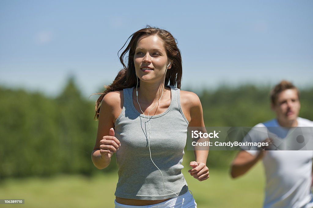 Summer jogging - Brown hair woman with headphones Brown hair woman with headphones jogging, man in background, shallow DOF Adult Stock Photo