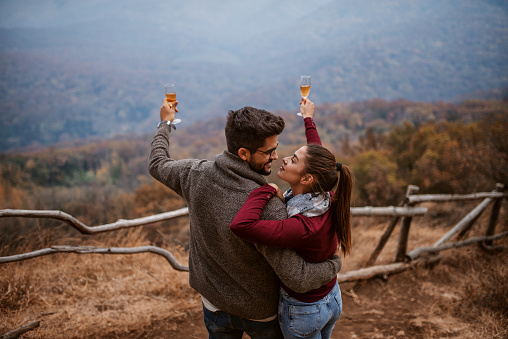 Couple hugging and holding glasses raised. Autumn time, rare view.