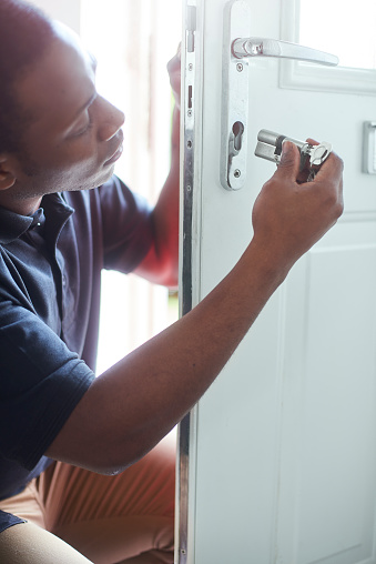A young locksmith changing the lock on a residential front door.