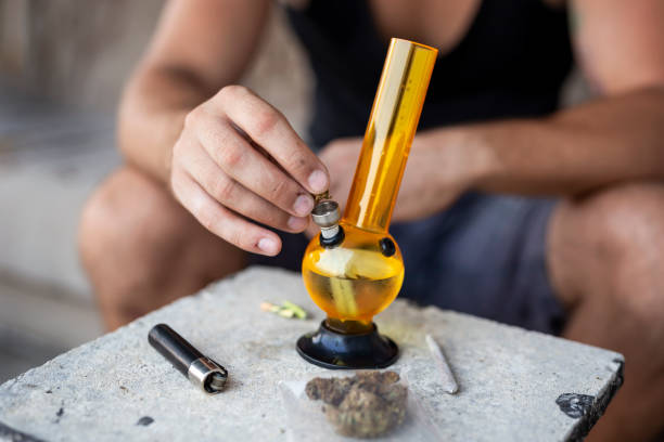 Man filling up bong with cannabis Young man smoking pot using bong; detail of male hand filling up bong with cannabis, getting it ready for use cannabis narcotic stock pictures, royalty-free photos & images