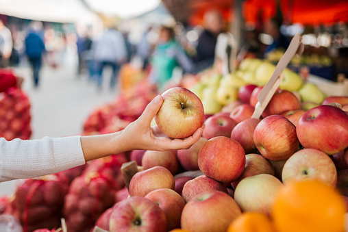 Close-up image of female hand holding apple at farmers market.