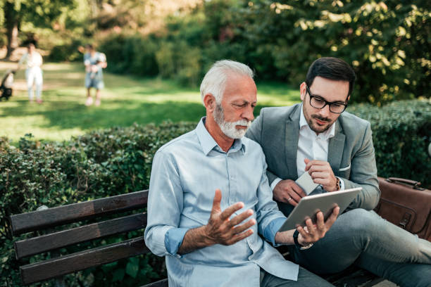 istock Two handsome business men looking at tablet while sitting on the bench. 1063921940