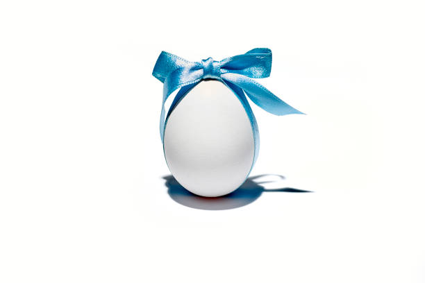 White egg and a curved ribbon on a light background, minimalist Easter greeting card with large copy space, selected focus, narrow depth of field