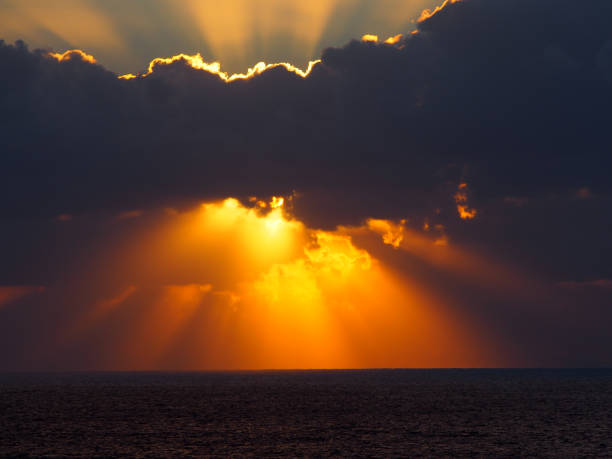 istock dramatic sunset over the sea with rays of light emerging from dark illuminated clouds over a calm ocean 1063942562