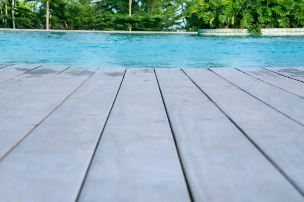 Closeup of wooden floor of swimming pool at the tropical resort with tropical trees background