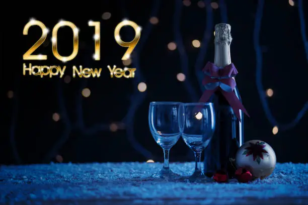 Red wine bottle with christmas ball and text of Happy New Year of 2019. Shot with snow on the table and bokeh background