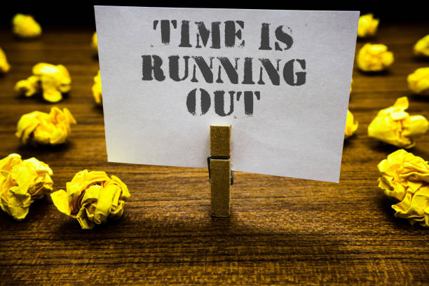 istock Text sign showing Time Is Running Out. Conceptual photo Deadline is approaching Urgency things cannot wait Paperclip grip white page with grey text woody floor laid blurry yellow lob. 1063948178